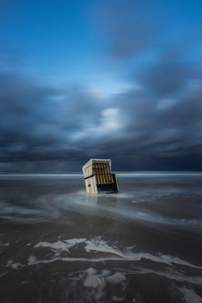 Long exposure of a lone beach chair partially submerged, under moody stormy sky.